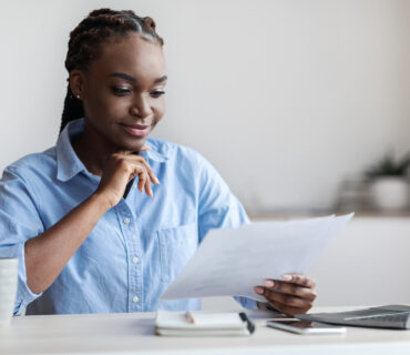 Ambitious Black Female Entrepreneur Working With Business Documentation In Office, Sitting At Desk, Checking Financial Report, Confident African Businesswoman Looking At Papers And Smiling, Free Space